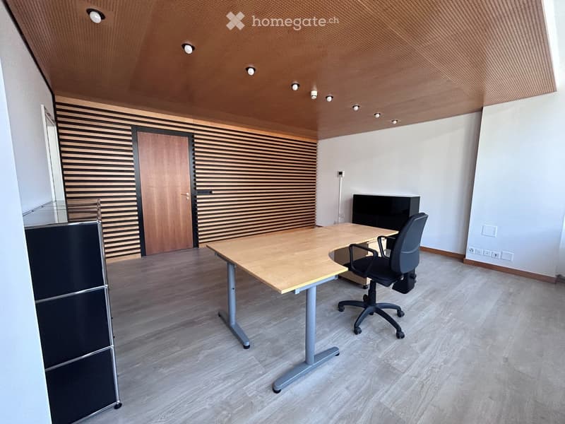 Modern office space with a wooden desk, ergonomic chair, and sleek black cabinet. The room features a contemporary design with a textured ceiling and minimalist decor.