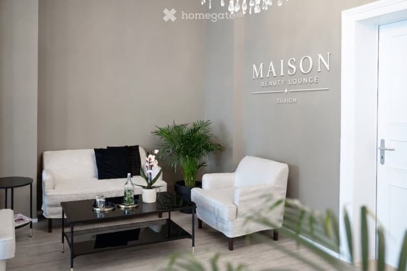 Modern, minimalist living room with a white sofa, coffee table, armchair, and decorative plants.