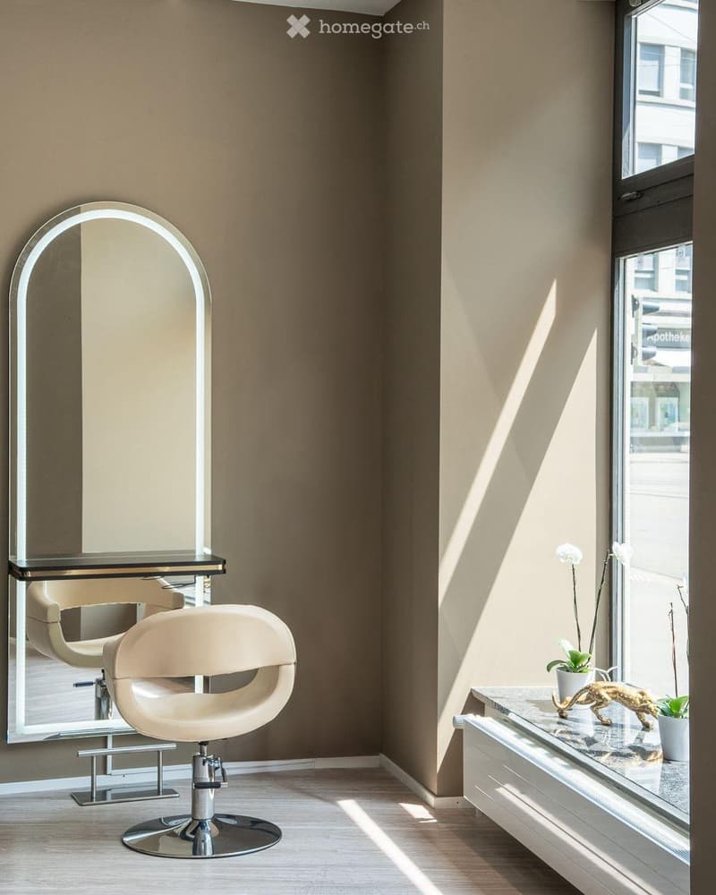 Modern, minimalist room with a large arched mirror, a sleek white chair, a small table with a plant and decorative sculpture, and natural light streaming through a large window.