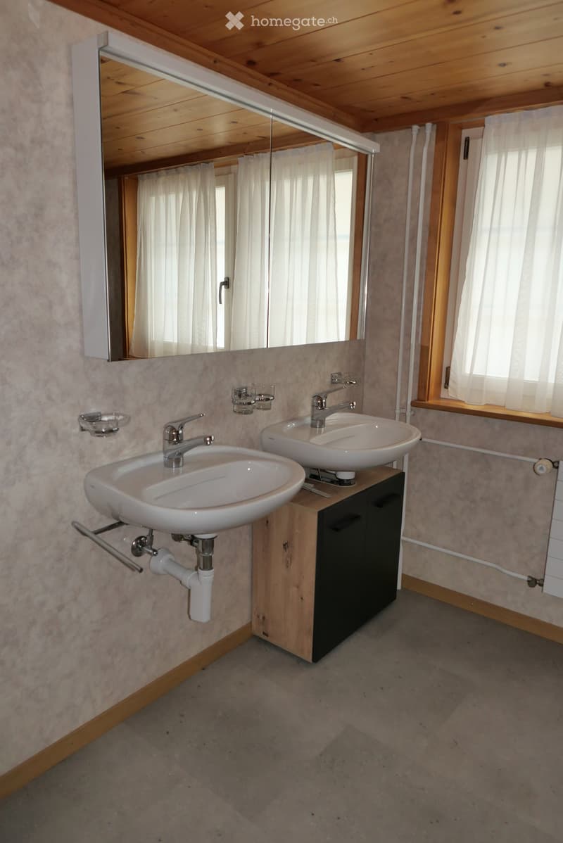 Bathroom with two white sinks, wooden cabinet, mirror, and light-colored walls.