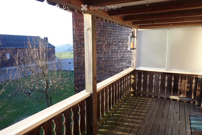 Wooden balcony with decorative railing, overlooking a grassy area and neighboring house.