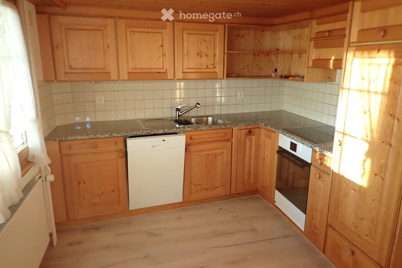 A cozy kitchen with wooden cabinets, a granite countertop, a sink with a faucet, a dishwasher, and an oven. The space is well-lit with natural light coming through a window on the left.