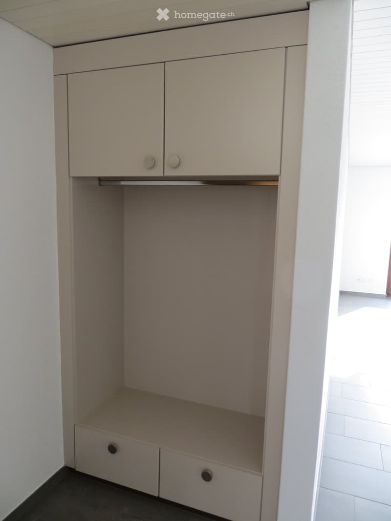 Empty built-in closet with two doors and two drawers, light-colored wood finish, white walls, and tiled floor.