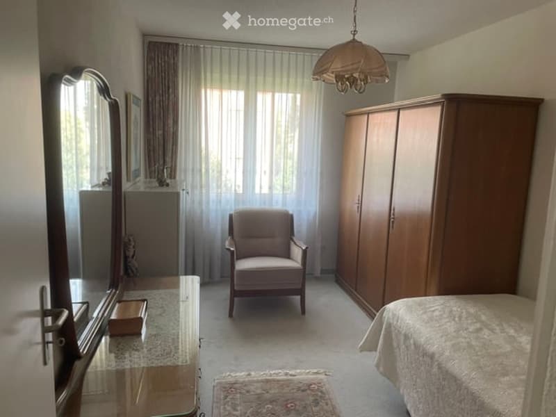 Bedroom with a bed, wardrobe, armchair, mirror, small table, and a hanging lamp.