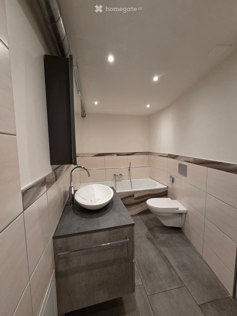 Modern bathroom with a white sink, chrome faucet, bathtub, and toilet. Features light-colored tiles and a sleek, contemporary design.