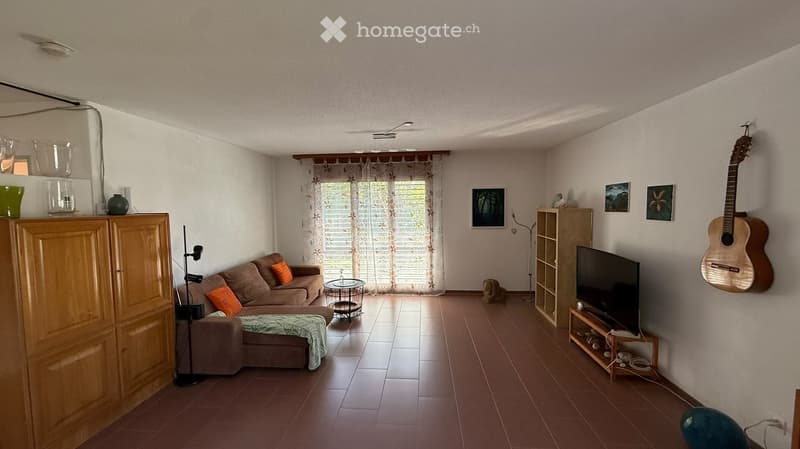 Living room with a brown sofa, coffee table, guitar on the wall, television, and decorative items on shelves.