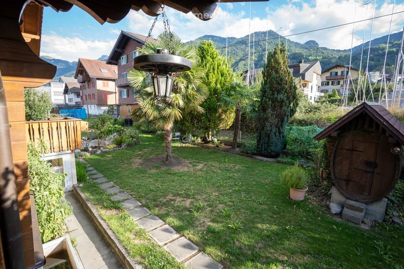 Garden with green grass, trees, a wooden deck, and a small wooden structure resembling a barrel.