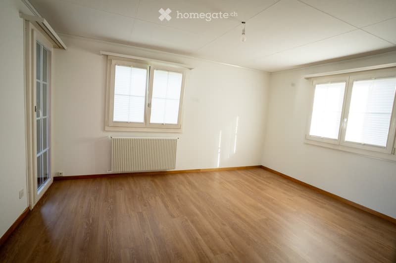 Empty room with wooden flooring, white walls, multiple windows, and a radiator. No furniture or equipment present.