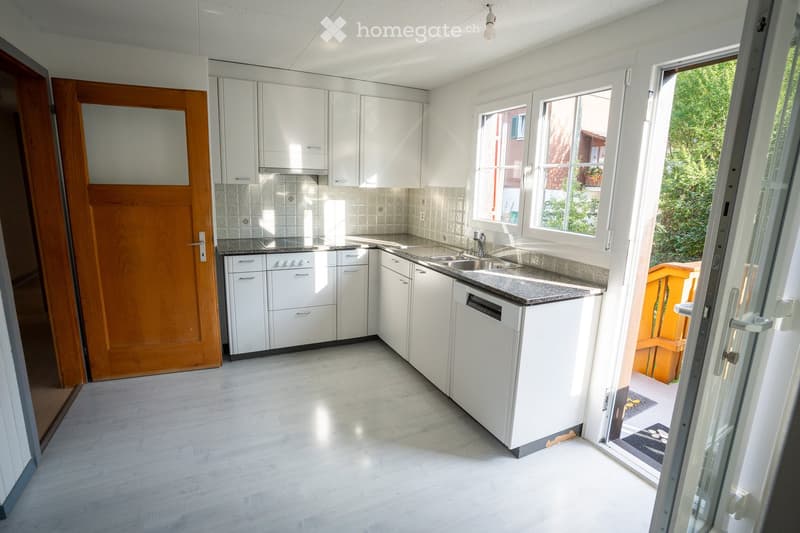 Bright, modern kitchen with white cabinets, granite countertop, stainless steel sink, and dishwasher. Large windows and sliding glass door lead to outdoor area.