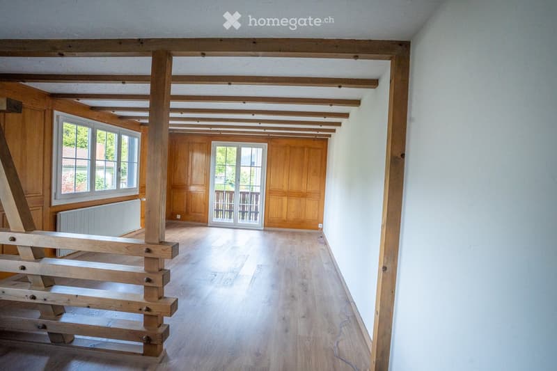 Empty room with wooden beams on the ceiling, wooden flooring, large windows, and a door leading to a balcony.