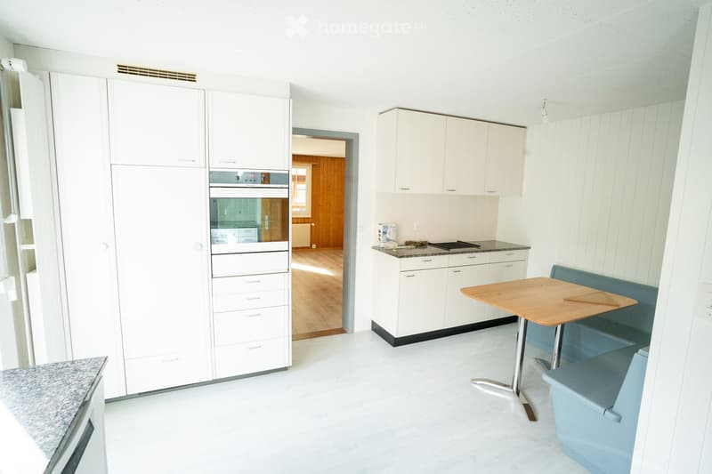 Modern kitchen with white cabinets, stainless steel appliances, granite countertops, and a small dining area with a table and bench.