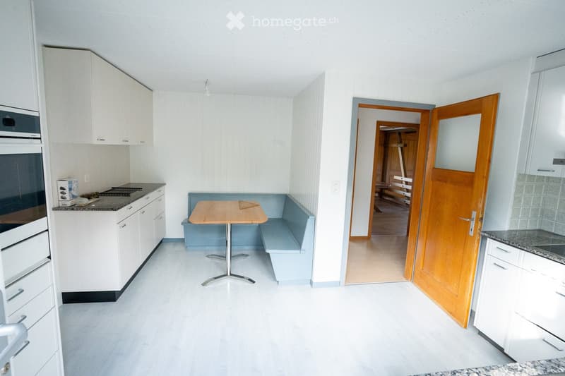 Modern kitchen with white cabinets, granite countertops, built-in oven, microwave, and a small dining area with a table and bench.