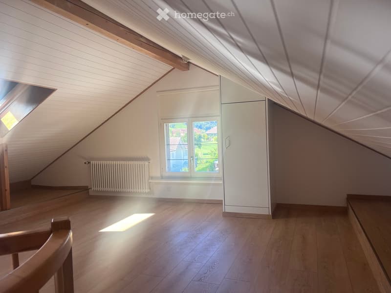 Empty attic room with wooden floors, white walls, skylight window, and built-in closet. Natural light streams in from the window and skylight.