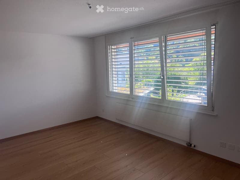 Empty room with wooden flooring, white walls, and large windows with blinds. A radiator is visible under the windows.