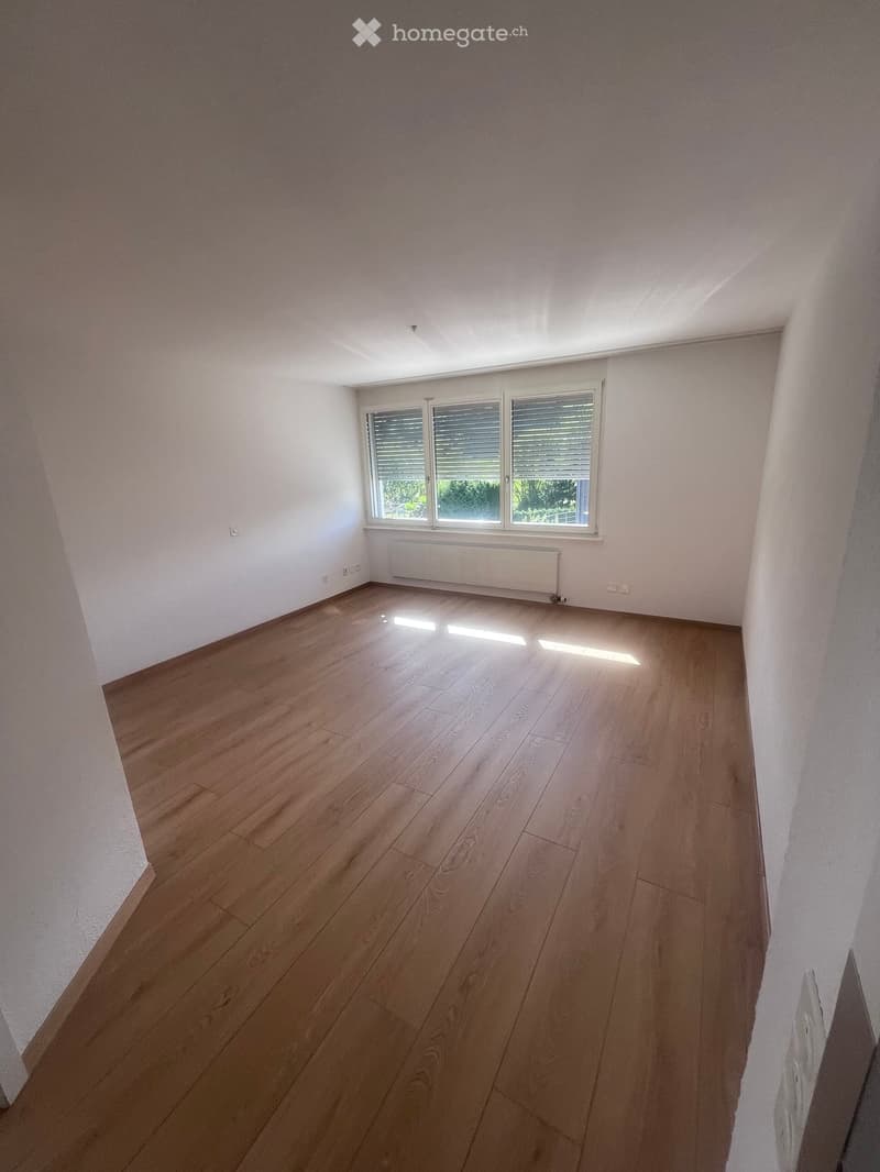 Empty room with wooden flooring, white walls, and large windows with blinds. No furniture or equipment present.