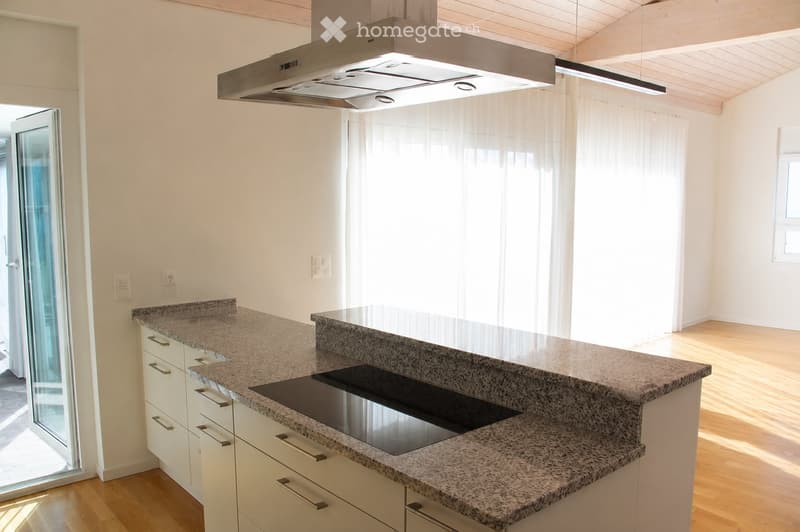 Modern kitchen with granite countertops, white cabinets, an induction cooktop, and a stainless steel range hood. Large windows with sheer curtains allow natural light to fill the space.