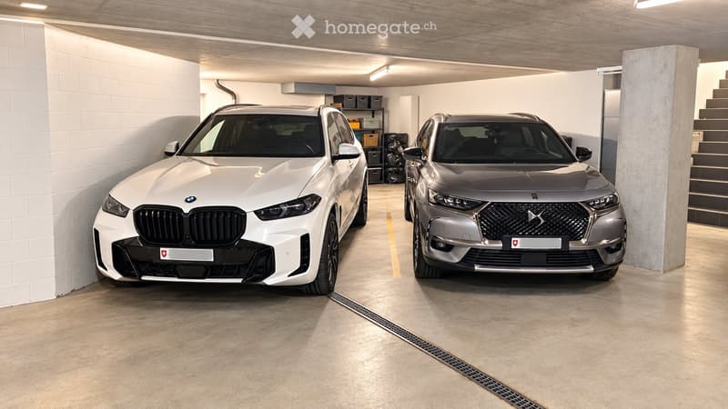 Underground garage with two parked cars, white brick walls, concrete floor, and storage shelves in the background.