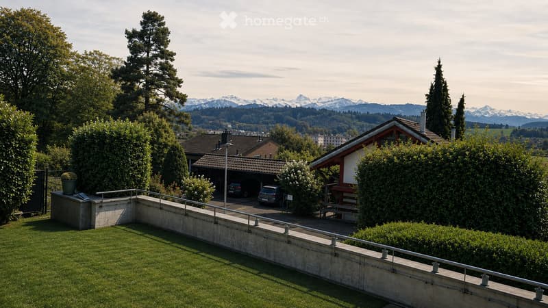 Garden area with a raised ground floor, a concrete wall, a metal railing, and a view of the surrounding houses and mountains.