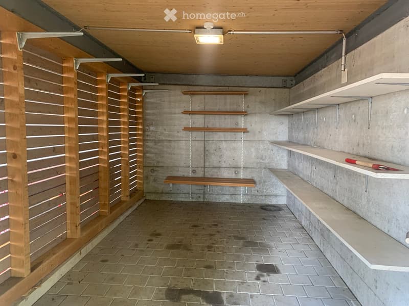 Empty storage room with wooden shelving units, concrete walls, tiled floor, and built-in benches.