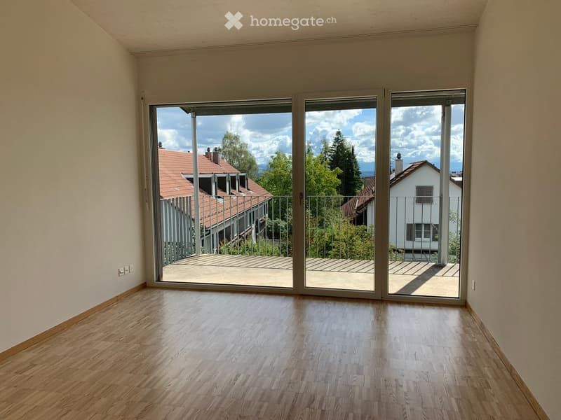 Empty room with wooden flooring and large sliding glass doors leading to a balcony with a view of the neighborhood.