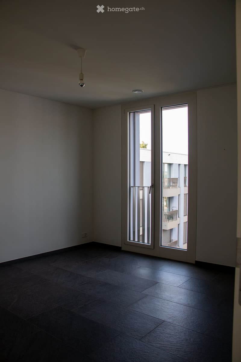 Empty room with dark tiled floor, white walls, and large sliding glass doors leading to a balcony.