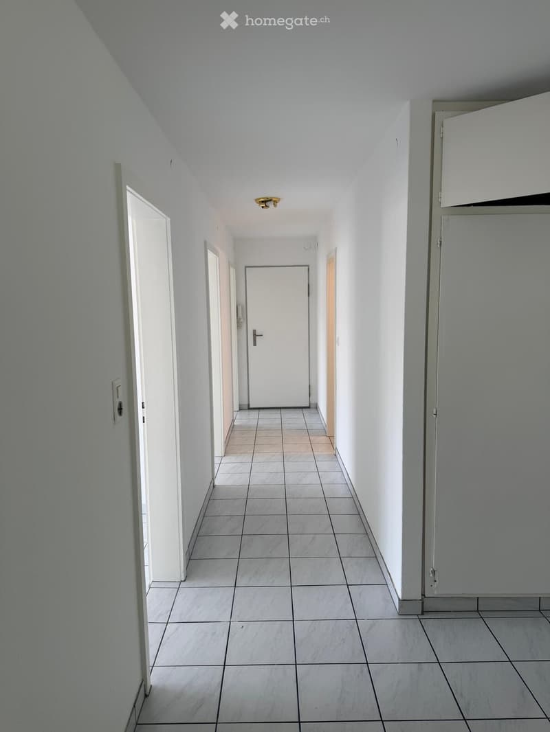 Empty hallway with tiled floor, white walls, and several doors leading to other rooms.