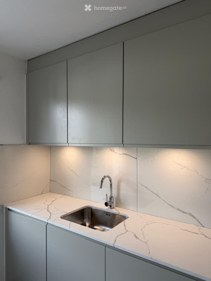 Modern kitchen with marble countertops, stainless steel sink, and sleek grey cabinets.
