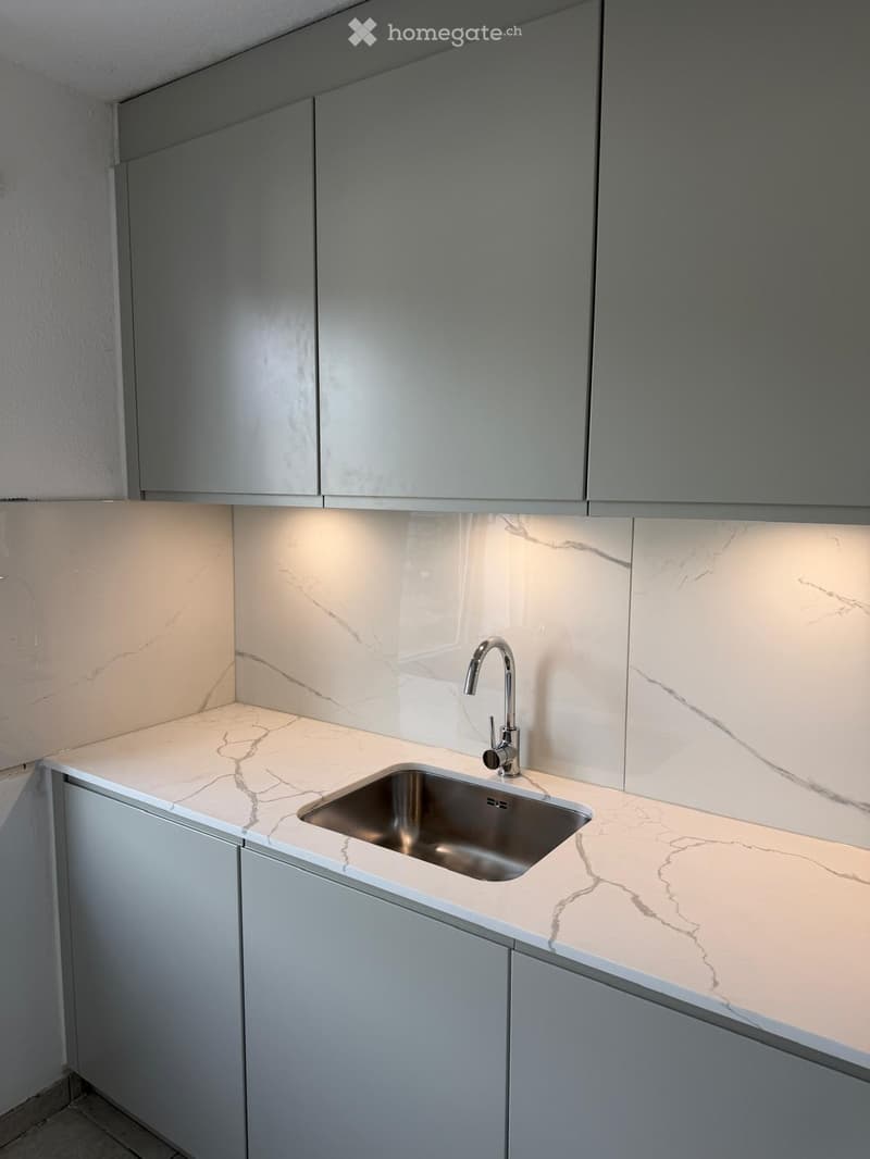 Modern kitchen with marble countertops, stainless steel sink, and sleek grey cabinets.