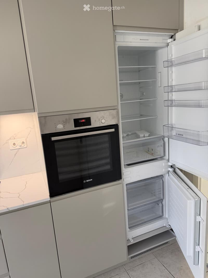 Modern kitchen with light-colored cabinets, a Bosch refrigerator with open doors, and a Bosch oven with a digital display.