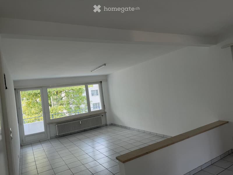 Empty room with white walls, tiled floor, large windows, and a wooden bench along one wall.