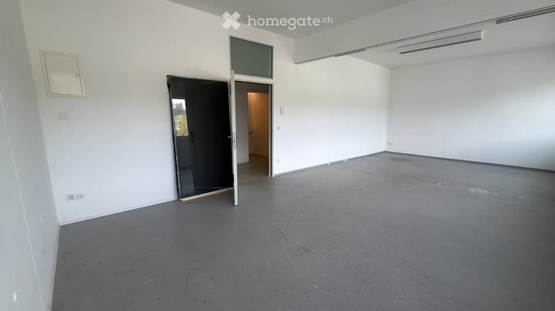 Empty room with white walls, grey concrete floor, and a partially open door leading to another room.