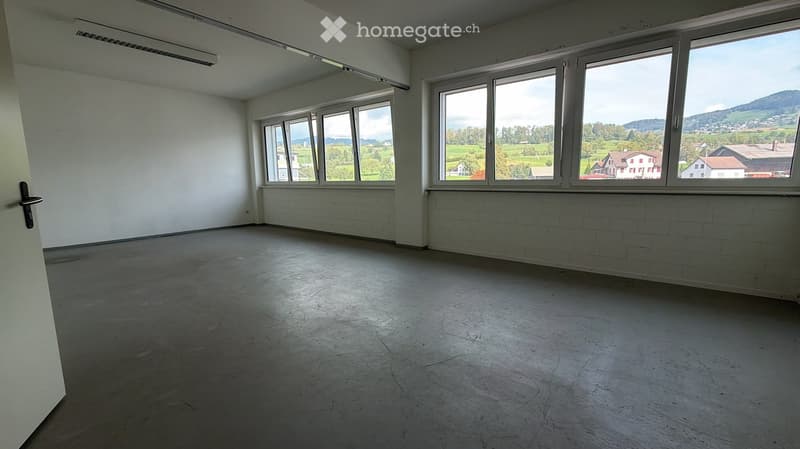 Empty room with bare walls, concrete floor, and large windows offering a scenic view of a valley and mountains.
