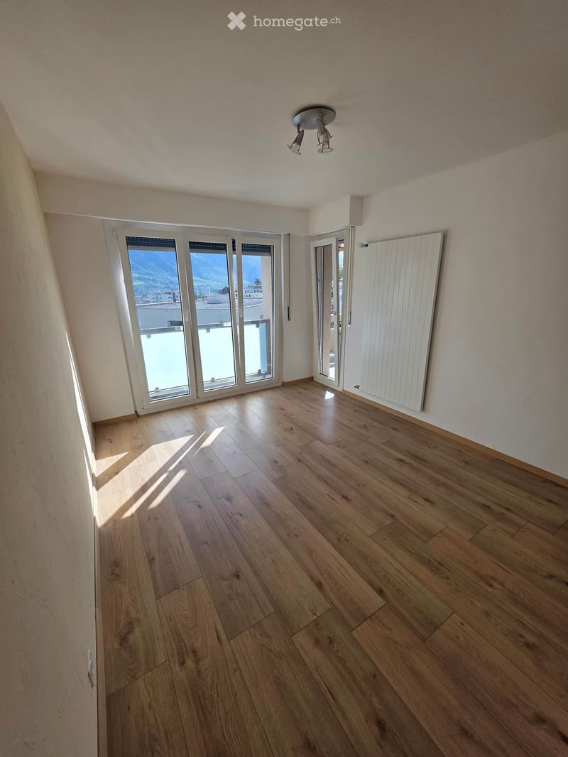 Empty room with wooden flooring, large windows, and a radiator on one wall.