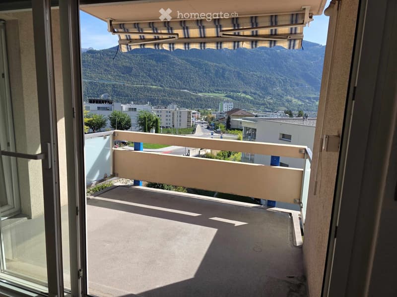 Balcony with a view of mountains and town, featuring a retractable awning and a railing.