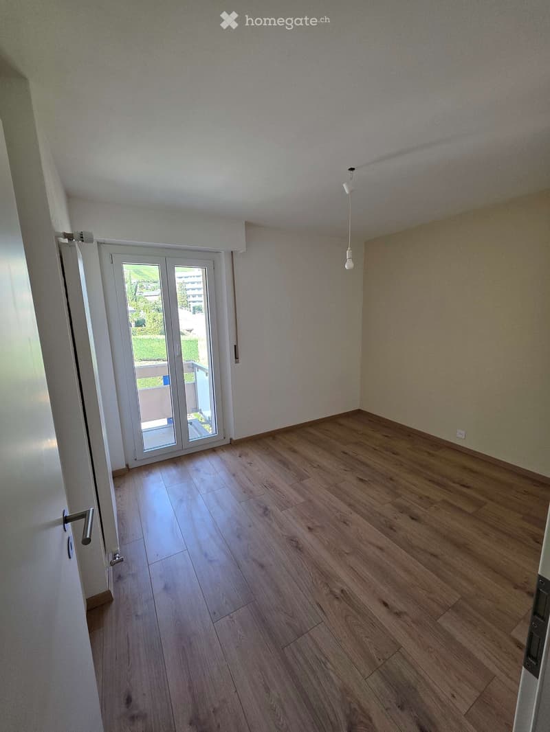Empty room with wooden flooring, white walls, and a large sliding glass door leading to a balcony.