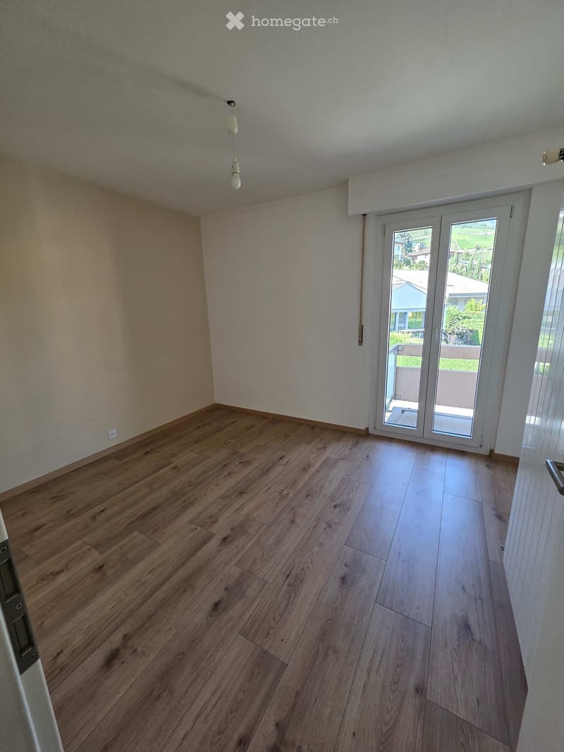 Empty room with wooden flooring, white walls, and a large sliding glass door leading to a balcony or outdoor area.
