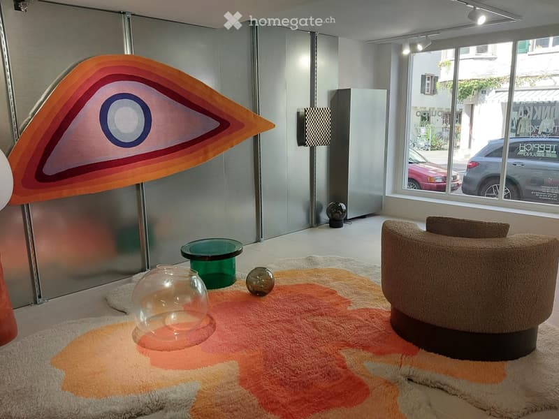 Modern living room with a round sofa, glass table, decorative vases, and a colorful rug.