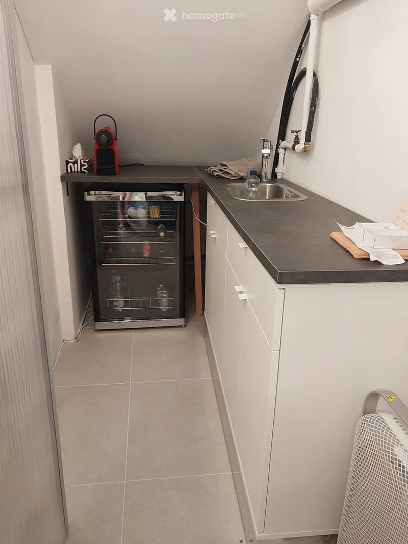 Compact kitchen with a stainless steel sink, white cabinets, a small refrigerator, and a coffee maker on the counter.