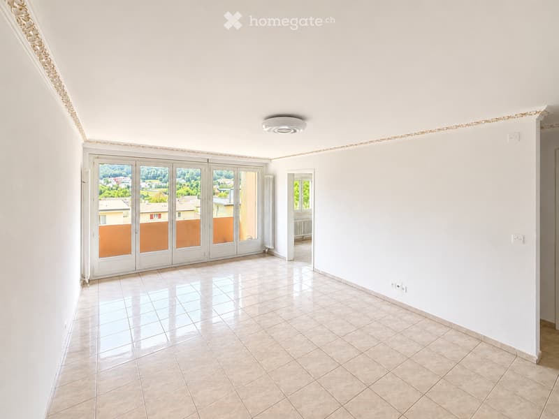 Empty room with tiled floor, white walls, large sliding glass doors leading to a balcony, and a small window on the side.