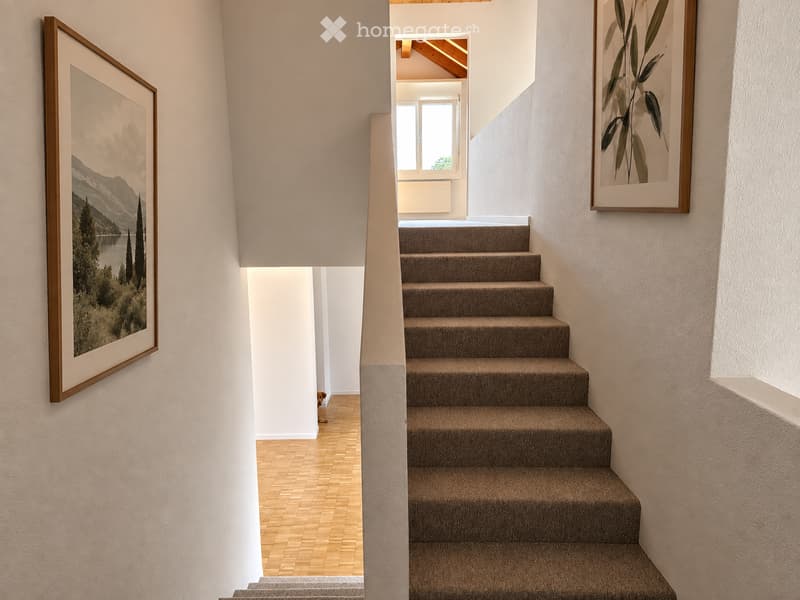 Staircase with carpeted steps and wooden handrail, flanked by white walls with framed artwork, leading to a bright room with wooden flooring and a window.