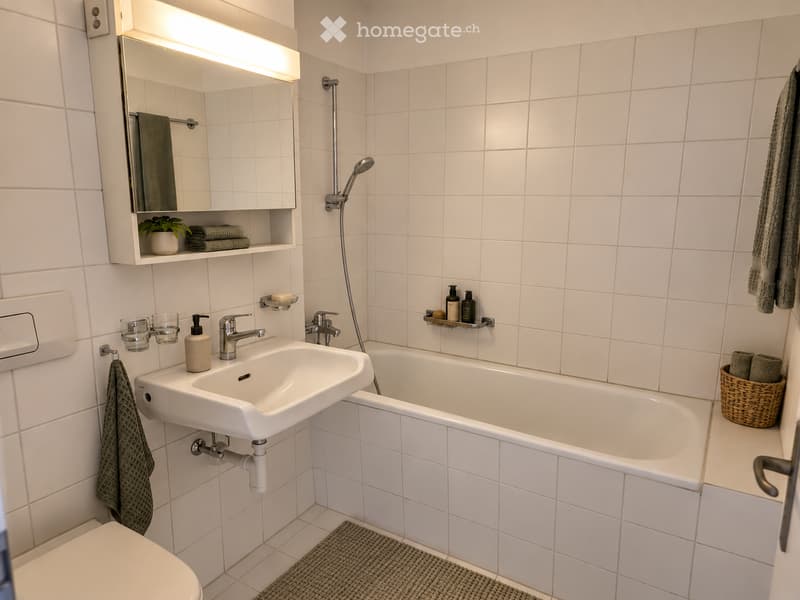 Modern bathroom with white tiles, a sink, bathtub, mirror, and neatly arranged towels and accessories.
