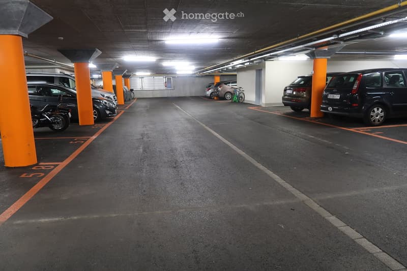 underground parking area with multiple cars parked, orange poles separating spaces