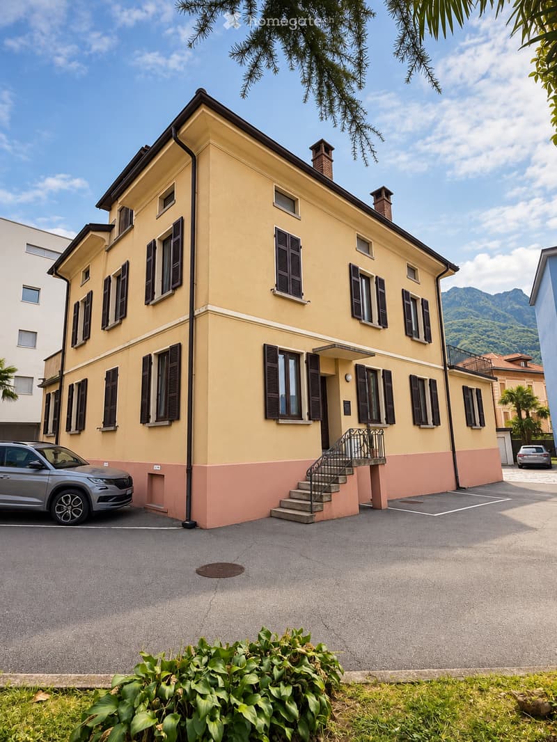 Two-story yellow house with black shutters, a small staircase leading to the entrance, and a parked car in front.