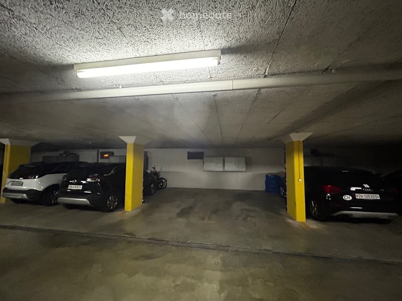 3 cars parked in parking garage, fluorescent light on ceiling, yellow and white pillars