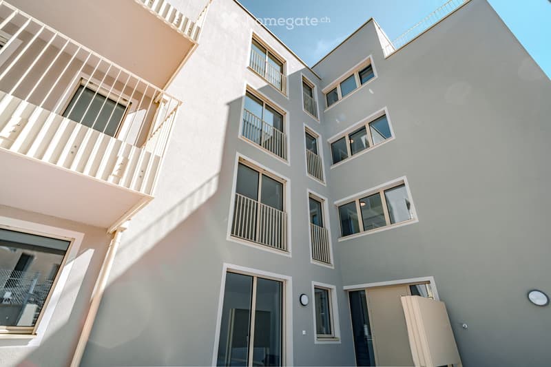 Modern multi-story building with light grey facade, multiple windows, and balconies with white railings.