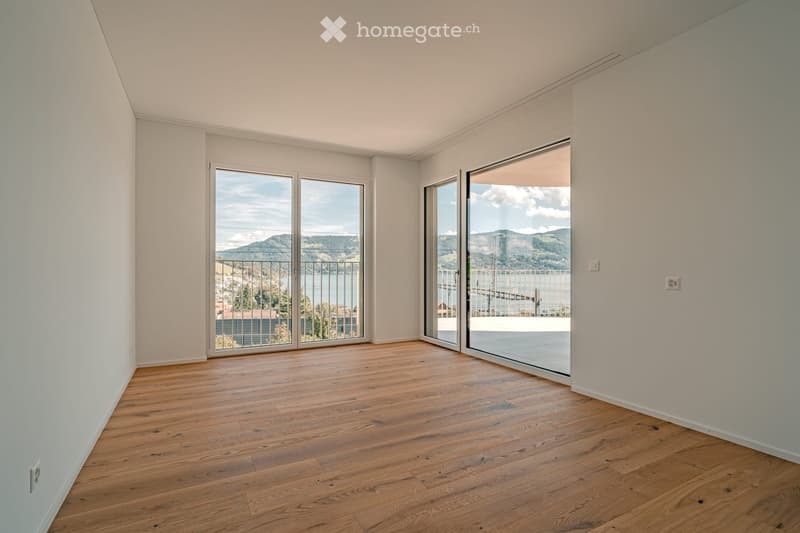 Empty room with wooden flooring, white walls, and large sliding glass doors leading to a balcony with scenic views.