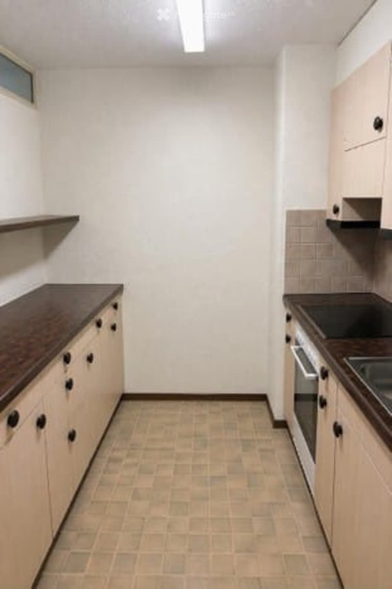 Modern kitchen with light-colored cabinets, dark countertops, and tiled flooring. Features an oven and a sink.
