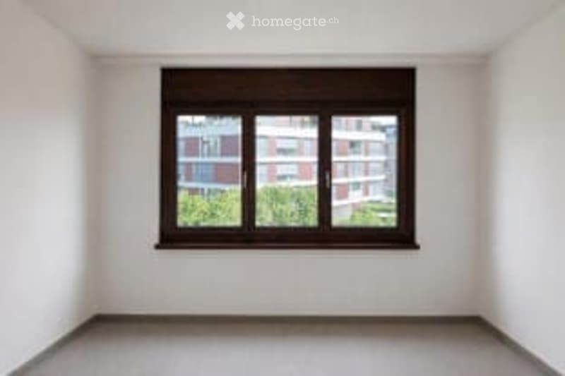 Completely empty room with white walls, grey floor, and a single window with black frame and blinds.