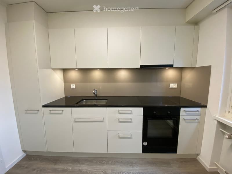 Modern kitchen with white cabinets, black countertops, a sink, and an oven.