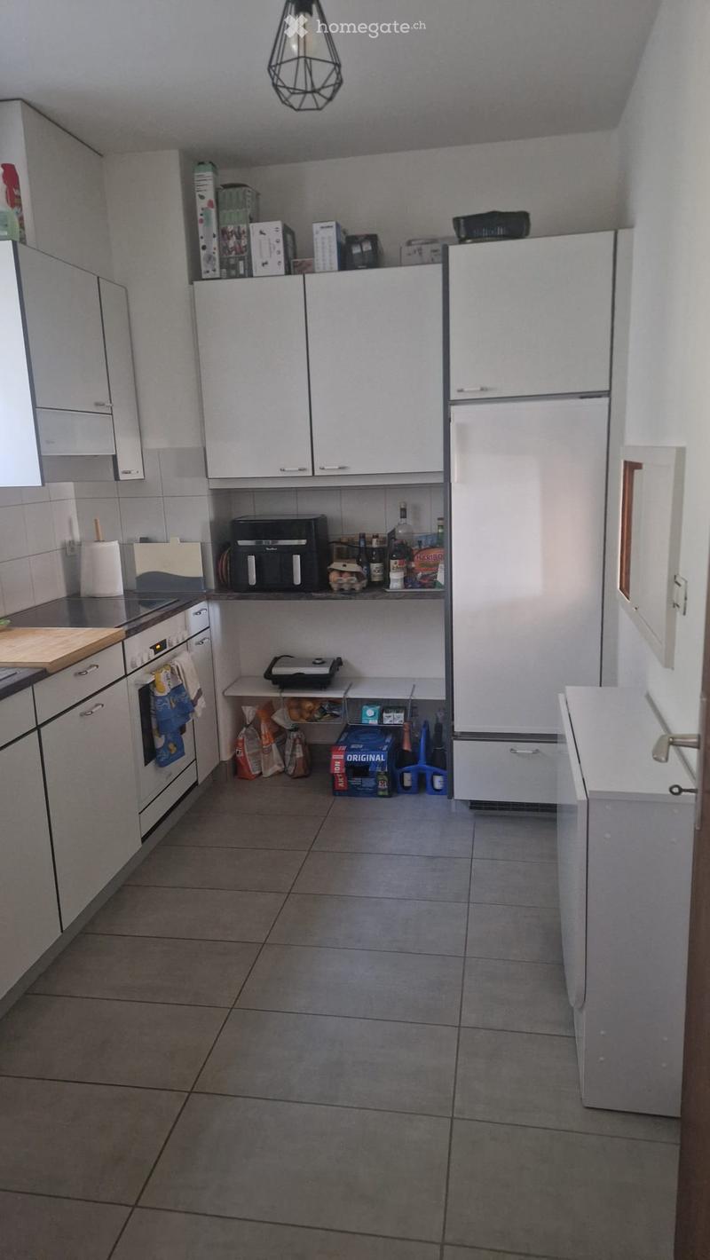 Modern kitchen with white cabinets, stainless steel appliances, tiled floor, and various items on the counter and shelves.
